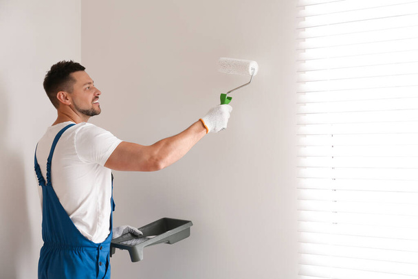 Man painting wall with white dye indoors - Foto, imagen