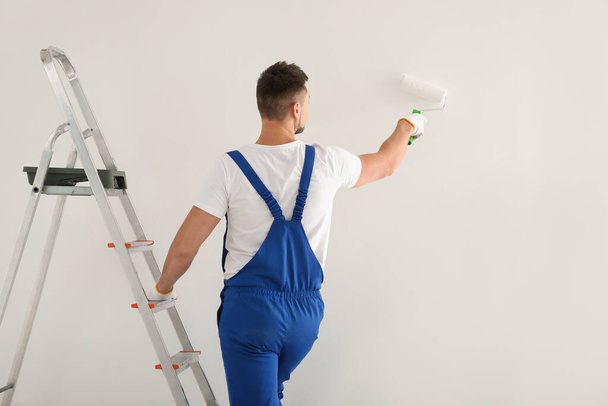 Άντρας ζωγραφίζει τοίχο με λευκή βαφή σε εσωτερικούς χώρους, πίσω όψη - Φωτογραφία, εικόνα