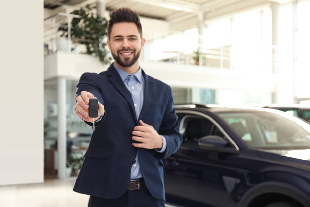 Salesman with key in modern car salon - Foto, imagen