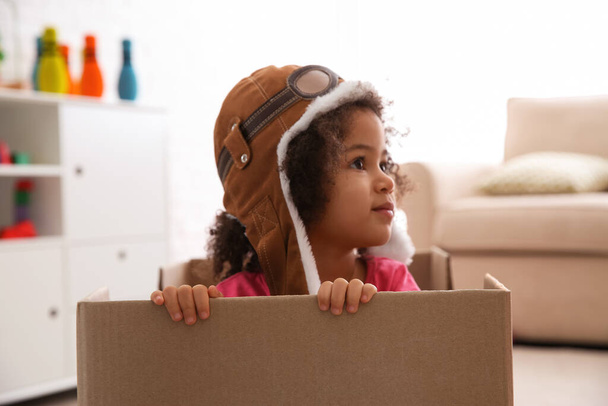 Cute African American child playing with cardboard box at home - Foto, imagen