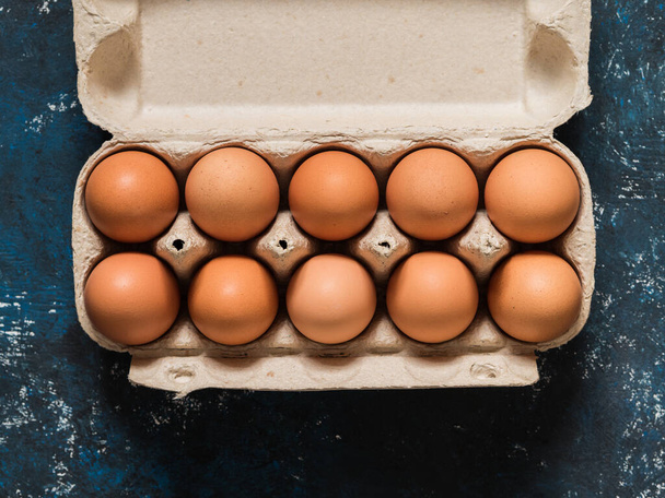 Πορτοκαλί αυγά κοτόπουλου σε ένα κουτί σε σκούρο μπλε φόντο. Η ιδέα του Πάσχα. Μινιμαλισμός. Στο πάνω μέρος. Αντιγραφή χώρου. - Φωτογραφία, εικόνα