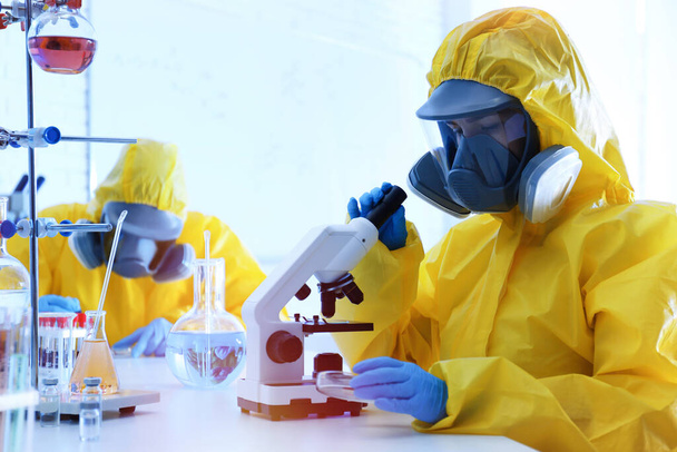 Scientist in chemical protective suit using microscope at laboratory. Virus research - Φωτογραφία, εικόνα