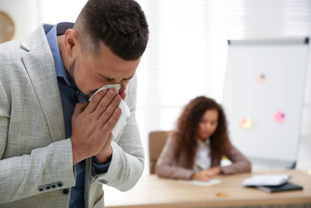 Sick man sneezing in office. Influenza virus - Valokuva, kuva