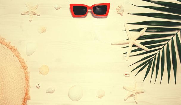 Yaz kompozisyonu güneş gözlüğü, hasır şapka, deniz yıldızı, kabuk ve ahşap masa üzerinde palmiye yaprağı. Tatil ve seyahat kavramı - Fotoğraf, Görsel