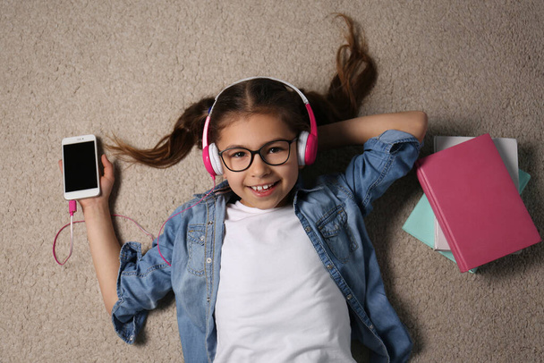Cute little girl listening to audiobook on floor, top view - Photo, image