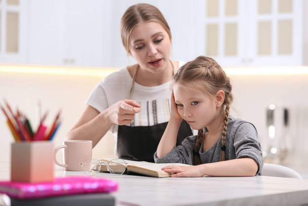 Woman helping her daughter with homework at table in kitchen - Photo, image