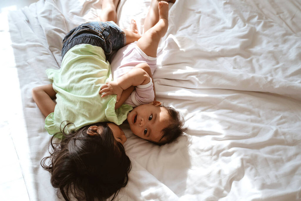 Aasialainen lapsi ja pikkusisko halaavat yhdessä valehdellessaan
 - Valokuva, kuva