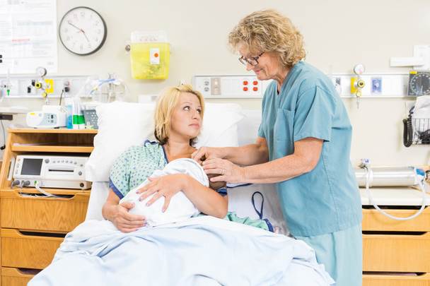 Улыбающаяся медсестра помогает женщине кормить грудью ребенка в больнице
 - Фото, изображение