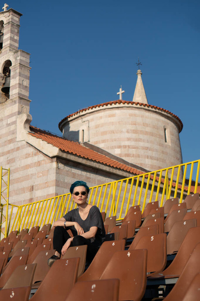 Das Mädchen mit den blauen Haaren sitzt auf einem Sportpodest vor dem Hintergrund der alten Kirche - Foto, Bild