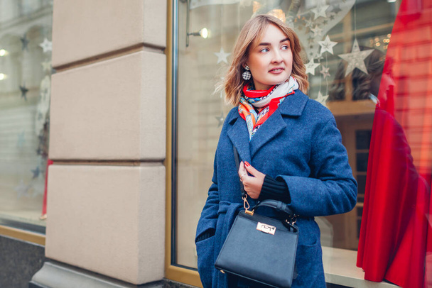 Стильна жінка в шарфі синього пальто тримає гаманець в магазині на вулиці на відкритому повітрі. Весняна мода жіночі аксесуари та одяг. Модне вбрання
 - Фото, зображення