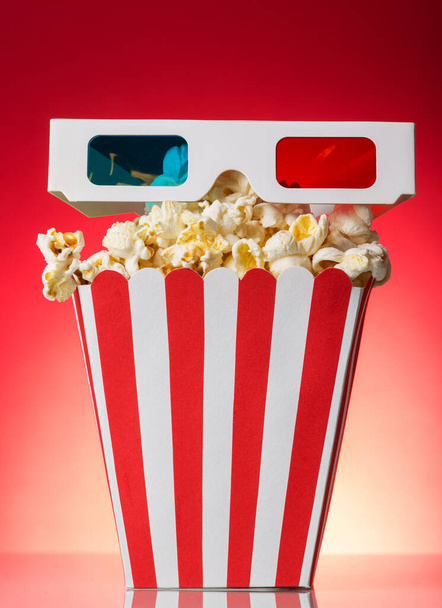 The square striped box with popcorn and 3D glasses on a red background - Photo, Image