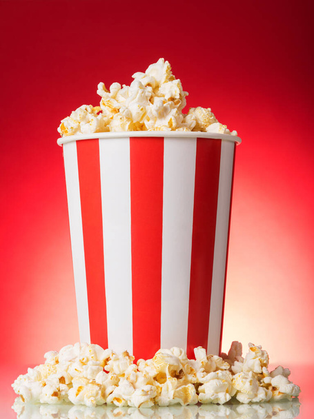 Salty popcorn in a large striped box on a bright red background - Zdjęcie, obraz
