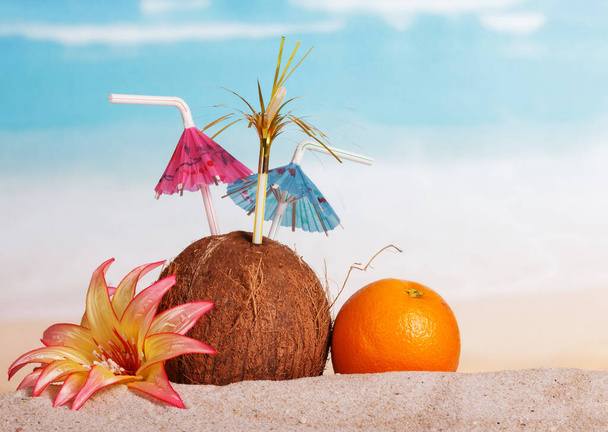 Coconut, orange and flower in the sand against the sea. - Fotoğraf, Görsel