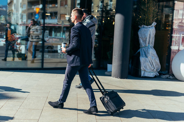 Young businessman walking through a station and pulling his travel bag. - Photo, Image