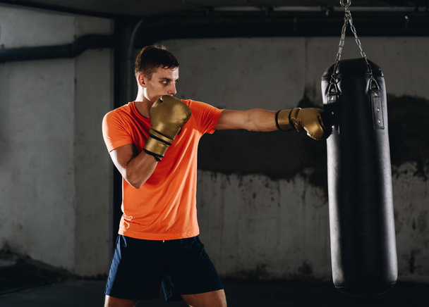 Homme sportif frappant un sac avec des gants de boxe à la salle de gym. Concept sport, fitness, arts martiaux - Photo, image