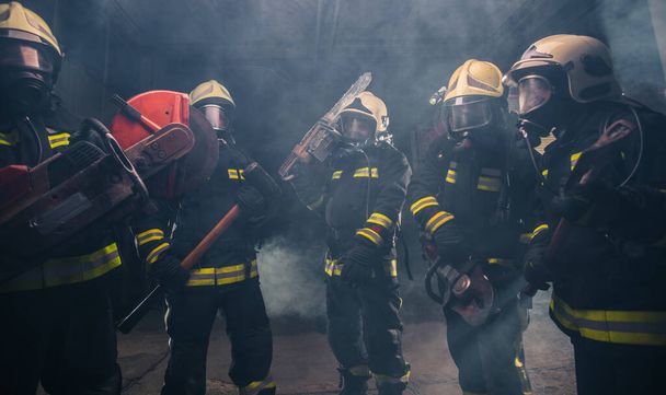 Grupo de bomberos con motosierra y martillo de trineo practicando en el garaje del departamento de bomberos - Foto, Imagen