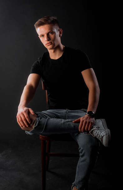 Cool young man dressed in black t-shirt and blue ripped jeans posing - Foto, afbeelding