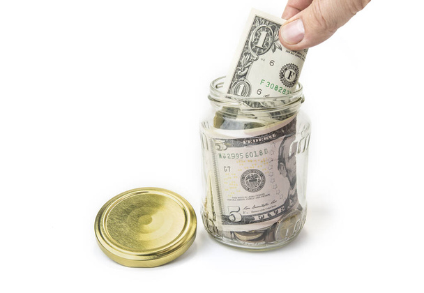 рука опускает деньги в стеклянную банку для экономии
 - Фото, изображение