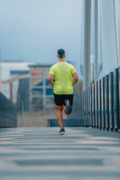 筋肉成熟した男以上40でスポーツウェアで橋の上を走る - 写真・画像