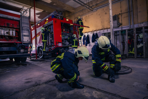 Пожарные готовят свою форму и пожарную машину на заднем плане внутри пожарной части.
 - Фото, изображение