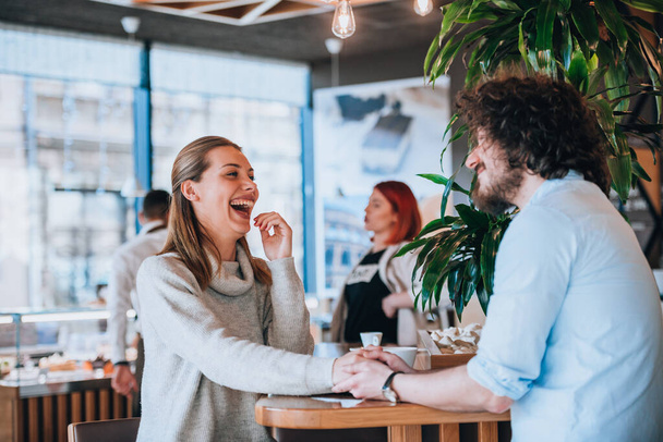 Młody mężczyzna i kobieta uśmiechają się i odbywają miłą rozmowę w kawiarni - Zdjęcie, obraz