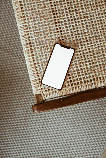 Blank screen smart phone on rattan chair. Flat lay, top view. Copy space mockup template. - Photo, Image