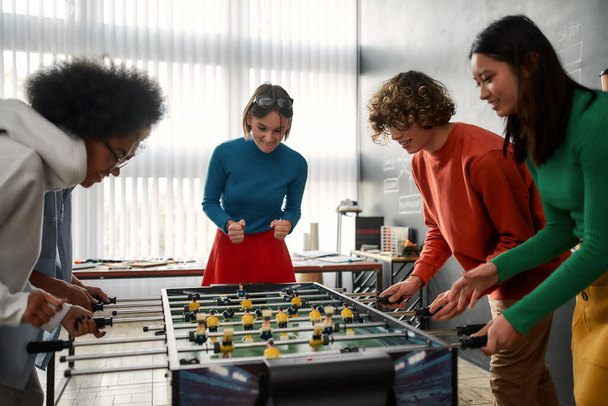 Together we are winners. Group of young and happy multicultural people in casual wear playing table soccer in the modern office. Office activities. Having fun together. Happy employees - Fotoğraf, Görsel