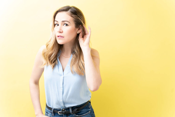 Caucasian attractive woman eavesdropping while standing against yellow background - Photo, Image