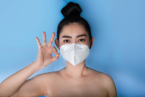 Zbliżenie kobiety zakładającej maskę respiratora N95 w celu ochrony przed chorobami układu oddechowego w powietrzu jako grypa covid-19 korona Pm2.5 kurz i smog, kobiecy gest kciuka w górę z wypisem ok - Zdjęcie, obraz