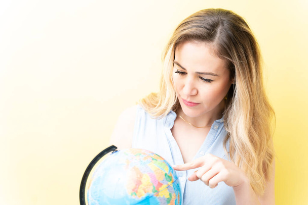 Beautiful adult woman pointing at globe against yellow background - Foto, Imagem
