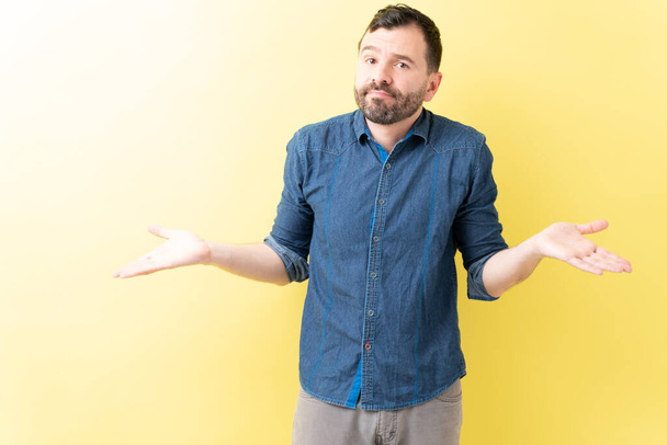 Homem adulto de pé com expressão confusa e sem noção contra fundo amarelo
 - Foto, Imagem