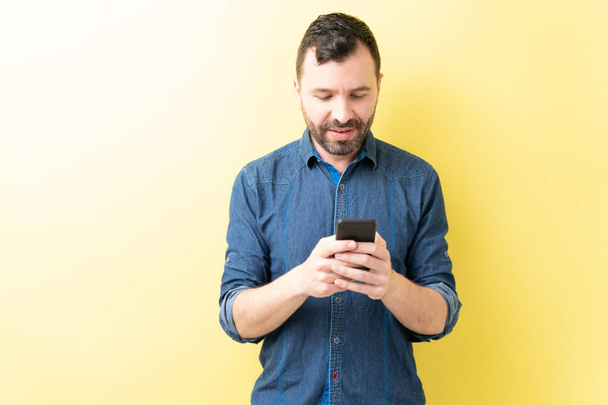 Latijnse volwassen man sms 'en via smartphone tegen gele achtergrond - Foto, afbeelding