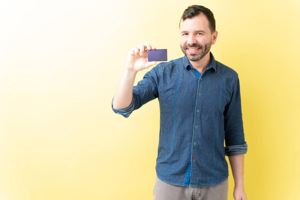 Lachende goed uitziende Spaanse man met creditcard over gele achtergrond - Foto, afbeelding