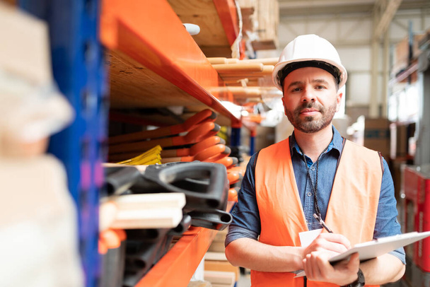Retrato del atractivo trabajador masculino que sostiene el portapapeles de inventario mientras está de pie en el almacén
 - Foto, Imagen