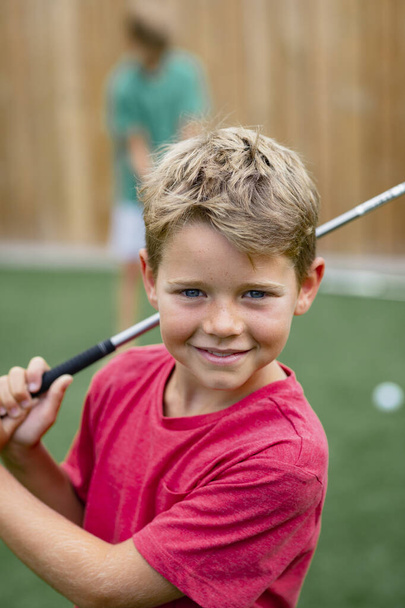 A front view shot of a young boy golfer smiling and looking at the camera, he is holding a golf club. - Foto, imagen