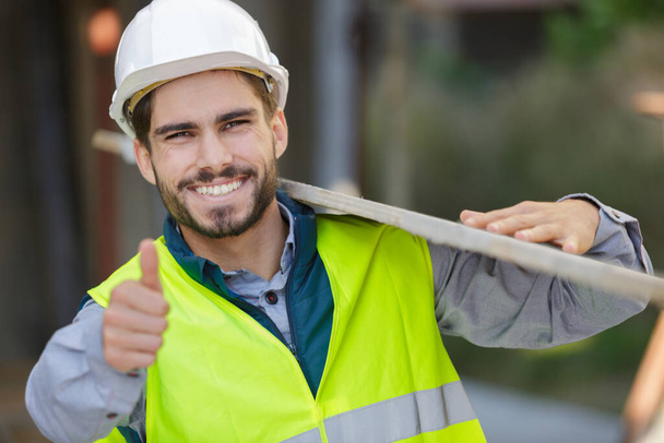 happy apprentice carrying wood on construction site - Foto, imagen
