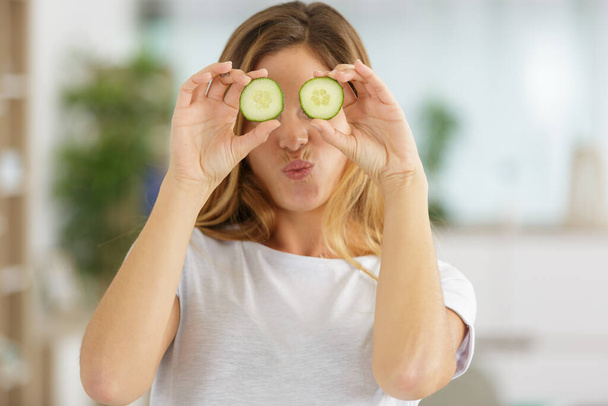 playful woman covering her eyes with slices of cucumber - Фото, зображення