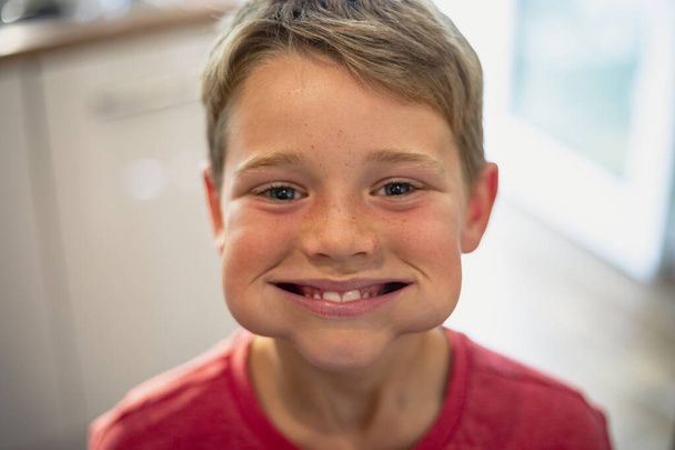 A front view shot of a young boy smiling and looking at the camera, he has a mouth full of cucumber. - Foto, Bild