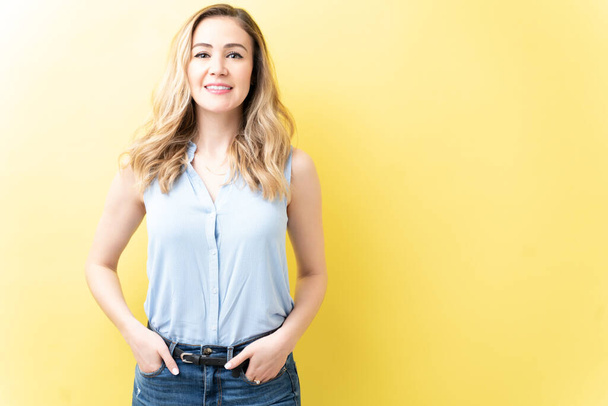Attractive Caucasian woman standing with hands in pockets over yellow background - Foto, Imagem