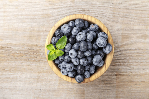 Juicy and fresh blueberries with green leaves on rustic table. Blueberry antioxidant. Concept for healthy eating and nutrition - Фото, изображение