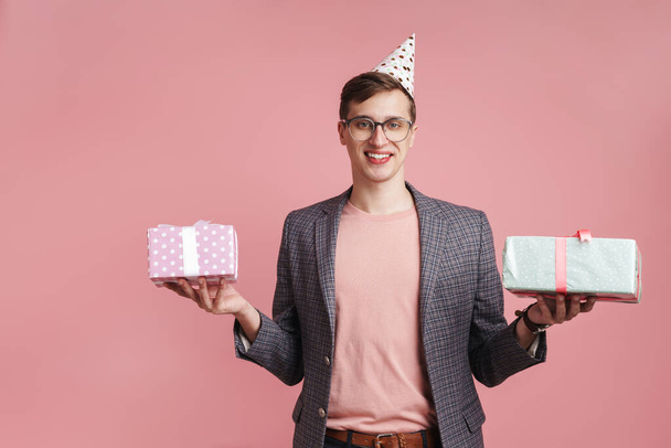 Immagine di un allegro ragazzo in bicchieri che tiene scatole regalo di compleanno isolato su sfondo rosa parete
. - Foto, immagini
