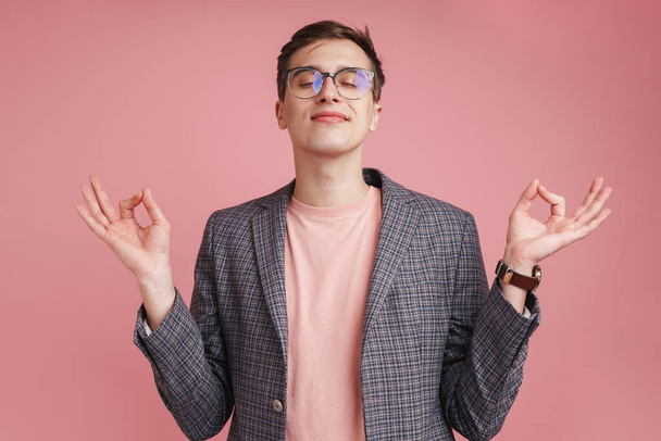 Photo of a young concentrated boy in glasses isolated over pink wall background make meditate calm gesture. - Фото, зображення