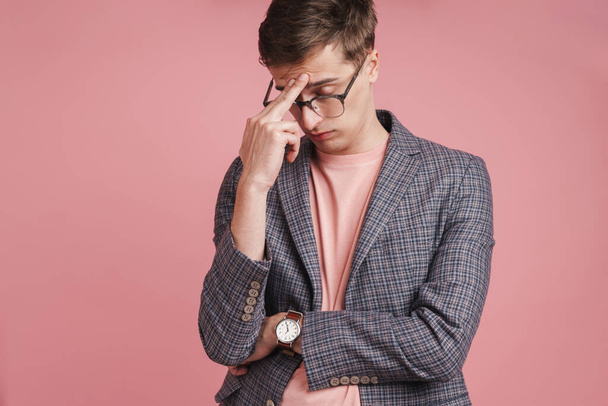 Image of a young stressed negative boy with headache in glasses isolated over pink wall background. - Fotografie, Obrázek