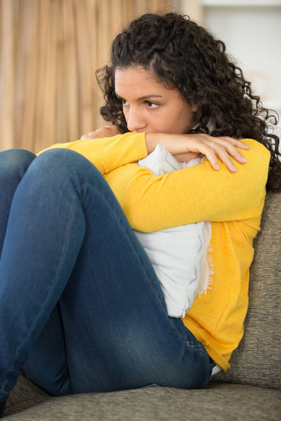 sad young woman sitting by sofa at home - Photo, Image