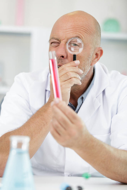 portrait mature male scientist holding magnifying glass in lab - Фото, изображение