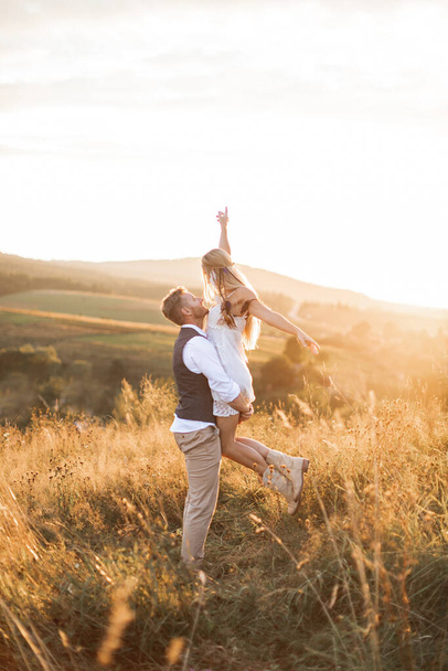 Shot of young boho hippie woman being carried by her handsome boyfriend in summer field. Couple having fun on their summer evening outdoors - Foto, afbeelding