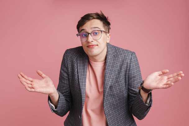 Portrait of a young confused attractive man wearing jacket standing isolated over pink background - Foto, imagen