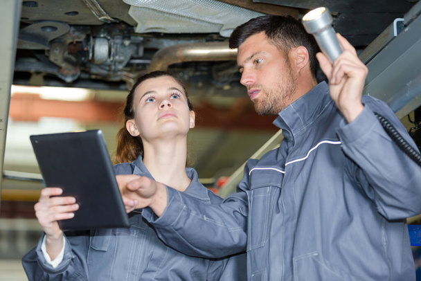 female and male mechanics standing underneath a car - Photo, image
