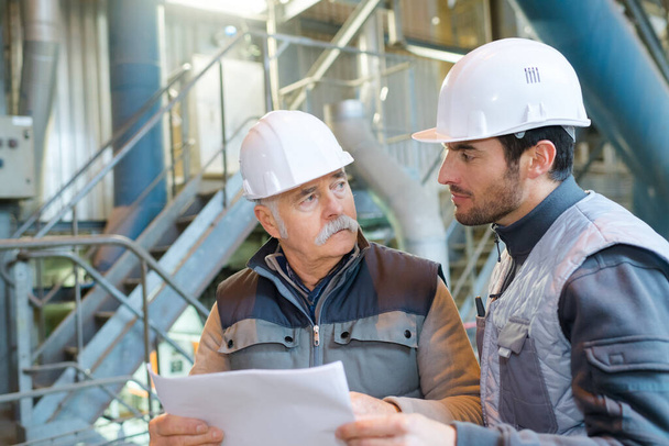 two male engineers in industrial manufacturing factory looking at plans - Foto, imagen