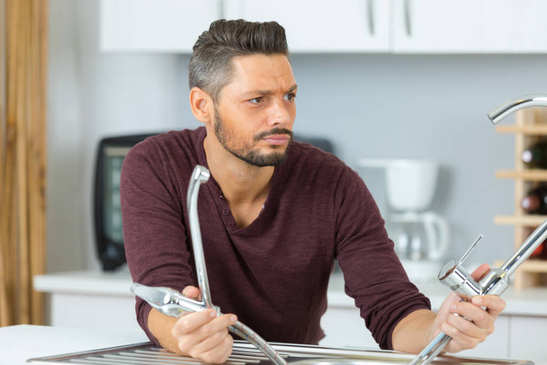 confused man fixing tap with wrench in the kitchen - Photo, image